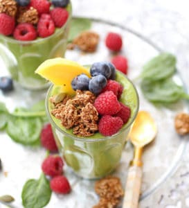 A glass of green smoothie topped with granola and fresh fruit