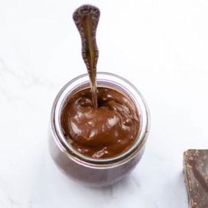A jar of luscious chocolate vegan pudding with a spoon in it.